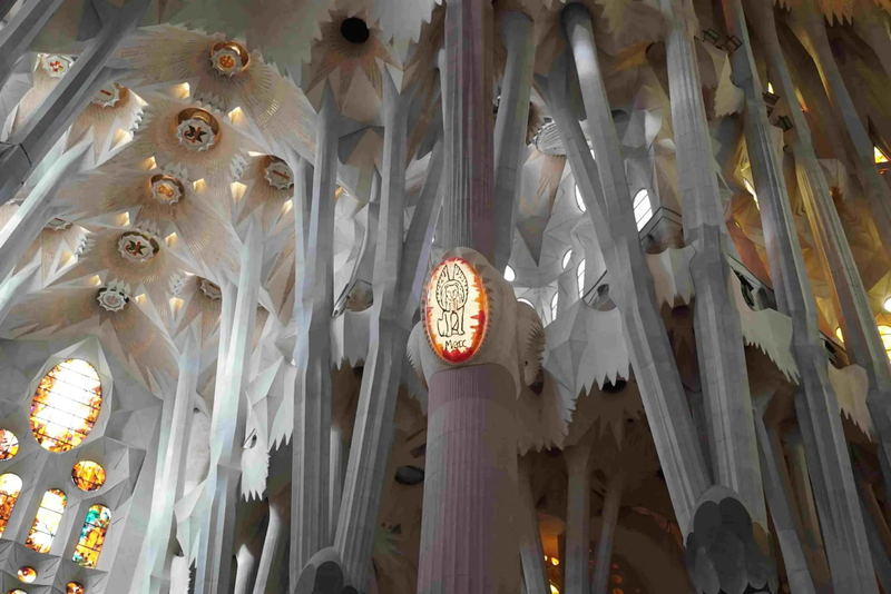 Interior view of a cathedral with tall, intricate columns reaching towards a detailed ceiling, featuring stained-glass windows.